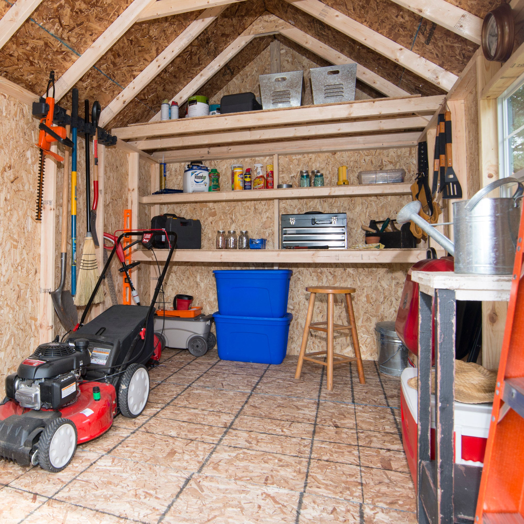 Interior of a storage shed with tools, shelves, a lawn mower, and storage bins. Interior of a storage shed with tools, shelves, a lawn mower, and storage bins.