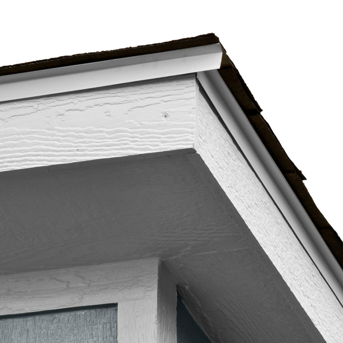 Close-up of a shed roof corner showing white trim, asphalt shingles, and textured wood siding.