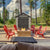 A shed with double doors, located in a backyard with red Adirondack chairs around a stone fire pit.