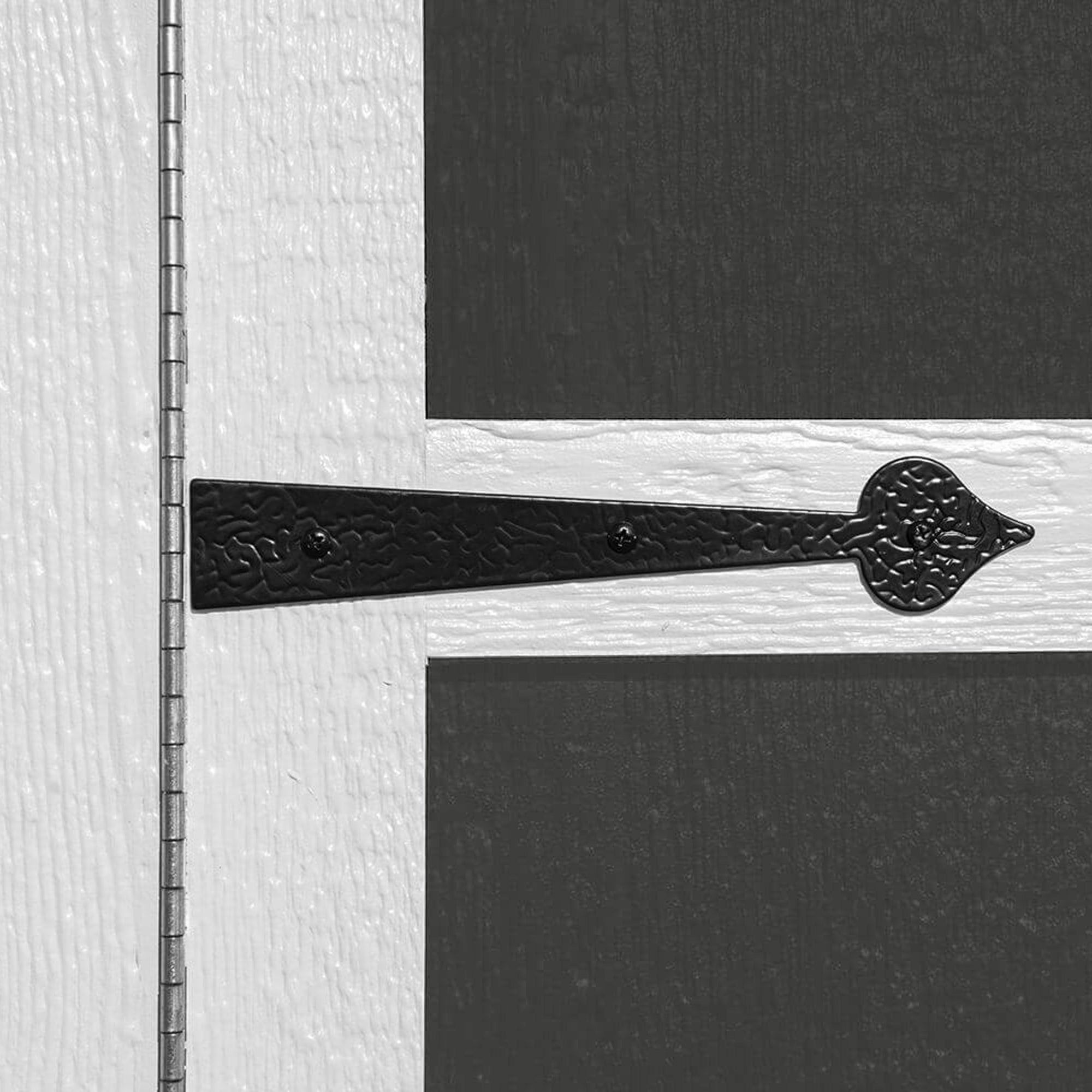 Close-up of a decorative shed door hinge with a textured black metal design.