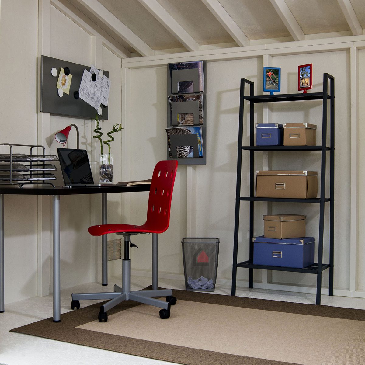  "Interior of a modern shed converted into a home office with a desk, red chair, shelving, and organized storage boxes