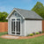 Storage shed with decorative double doors, a dormer window, and a landscaped yard.